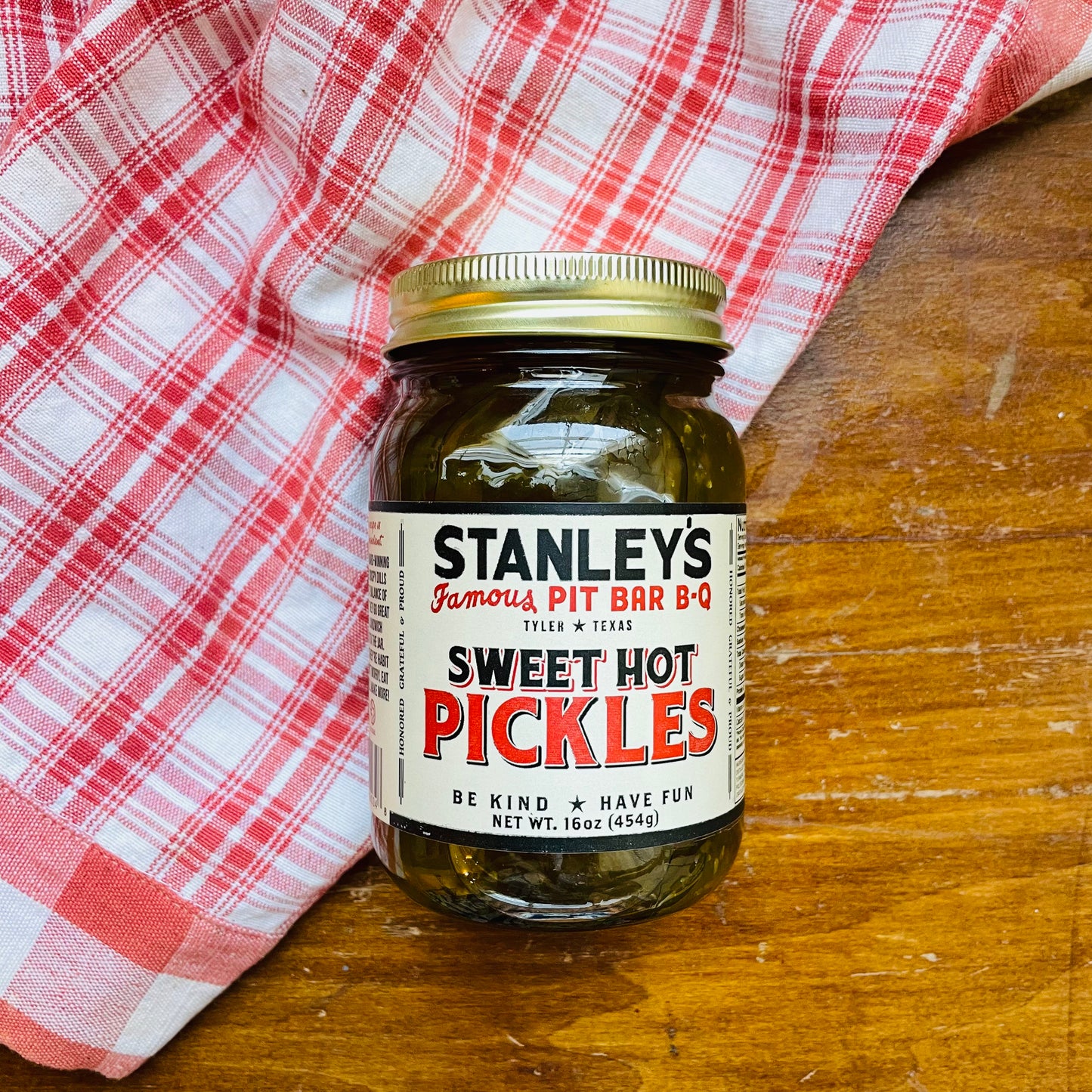 A jar of Stanley's Famous Sweet Hot Pickles on a wooden surface with a red and white checkered cloth. Pickles from Tyler, Texas bbq joint.