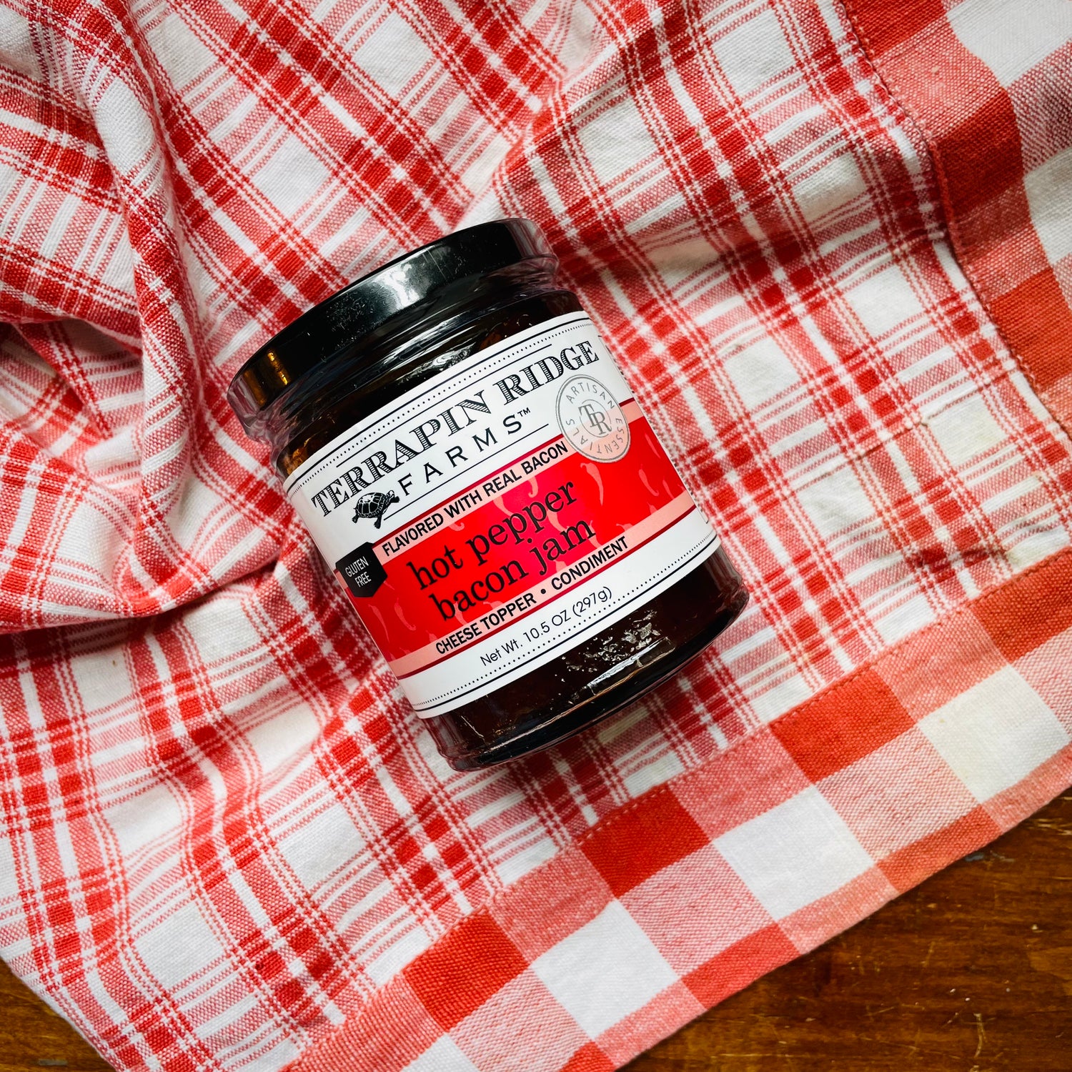A jar of Hot Pepper Bacon Jam on a red and white checkered cloth. Sweet but spicy jam that goes well with cream cheese. 