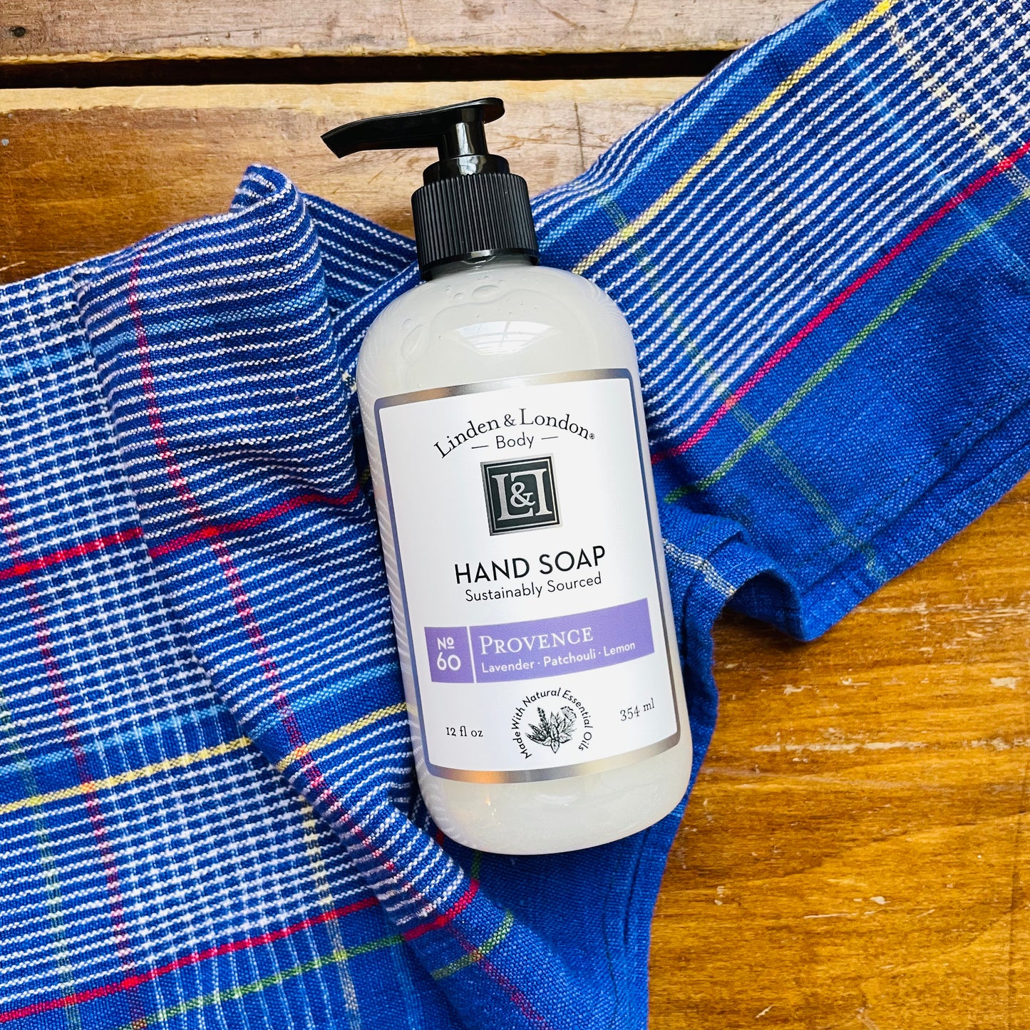 A pump bottle of Linden & London hand soap resting on a blue and red plaid cloth. Hand soap that smells like lavender, patchouli and lemon