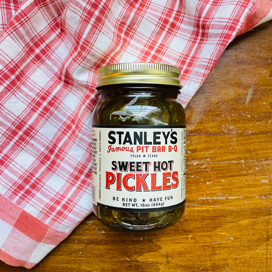 A jar of Stanley's Famous Sweet Hot Pickles on a wooden surface with a red and white checkered cloth. Pickles from Tyler, Texas bbq joint. 