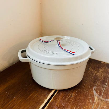 White truffle Staub cast iron dutch oven pot on a wooden table with a white wall background