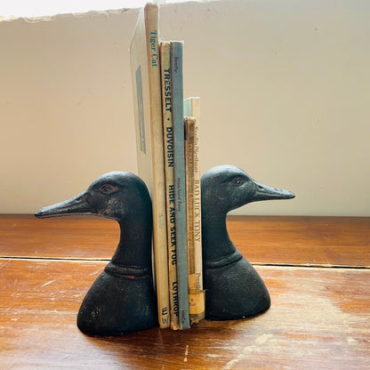 Two black cast iron duck head bookends placed on a wooden surface, holding up a couple of books.