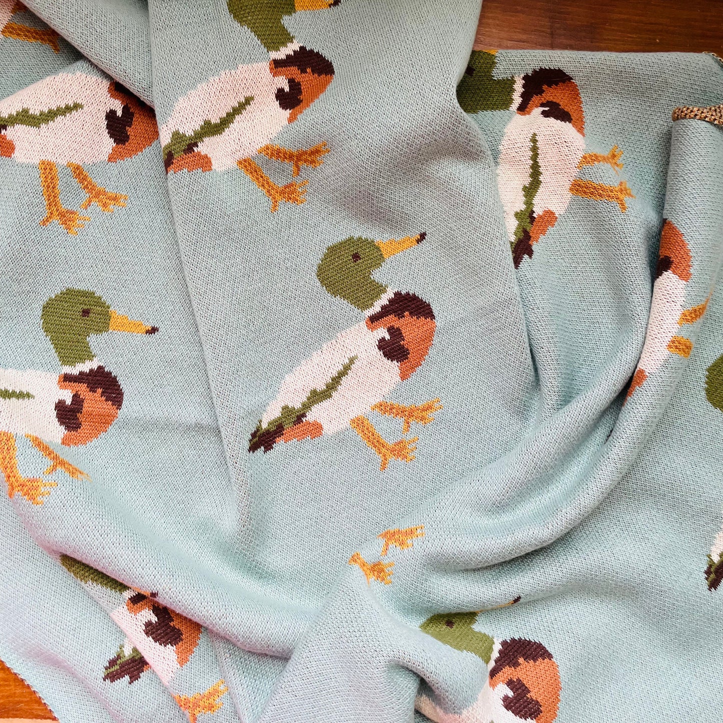 A blue cotton knit blanket with a pattern of ducks in various poses.