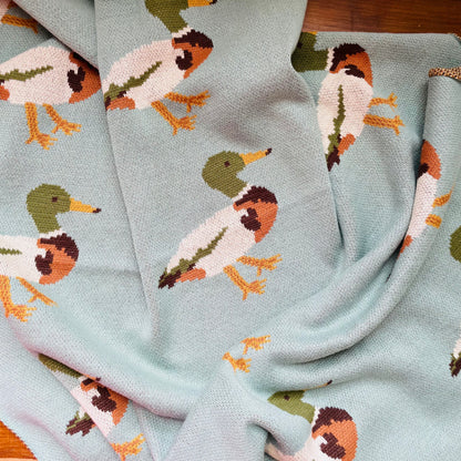 A blue cotton knit blanket with a pattern of ducks in various poses.