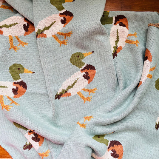 A blue cotton knit blanket with a pattern of ducks in various poses.