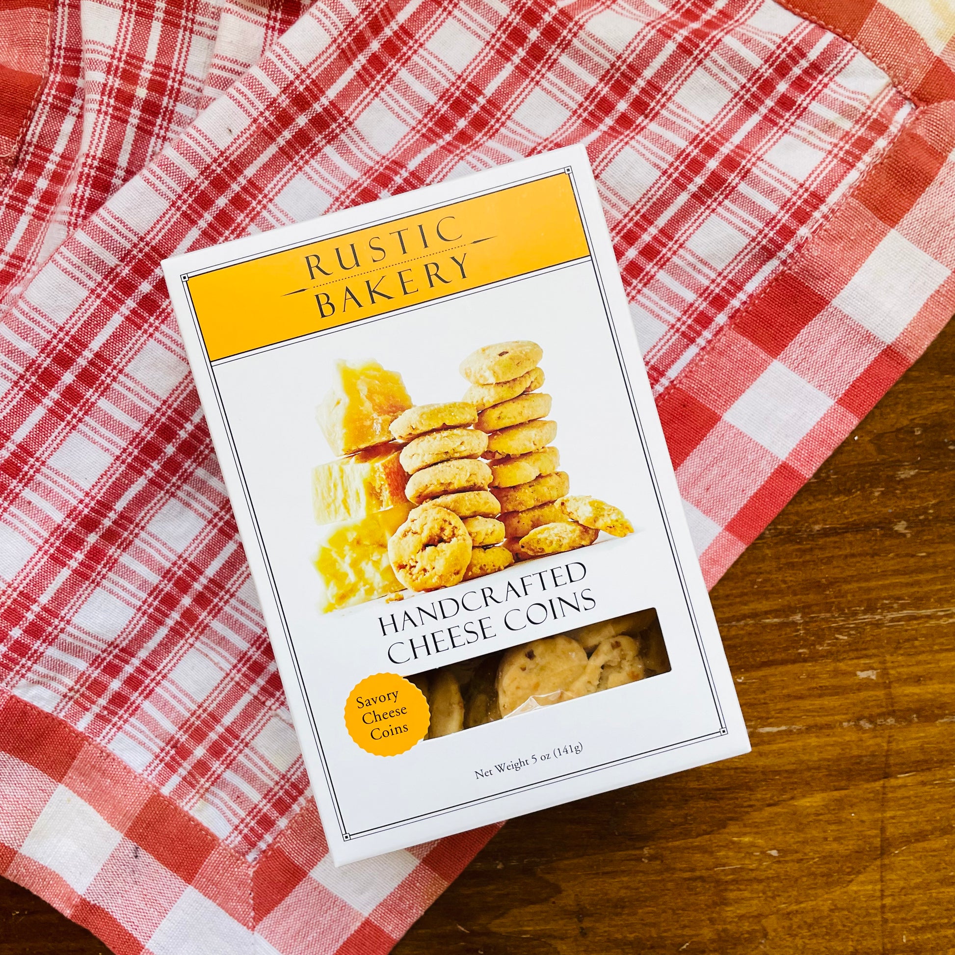 A packaged box of Savory Cheese Coins on a red and white checkered cloth.